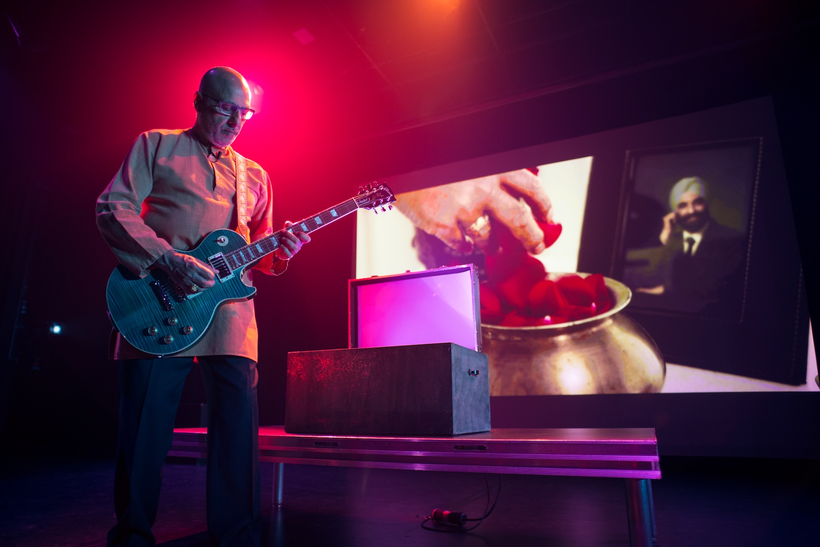Himmat Singh Shinhat performing Panj — playing electric guitar on stage with video projection of his father's photograph in the background © Laurence Ly