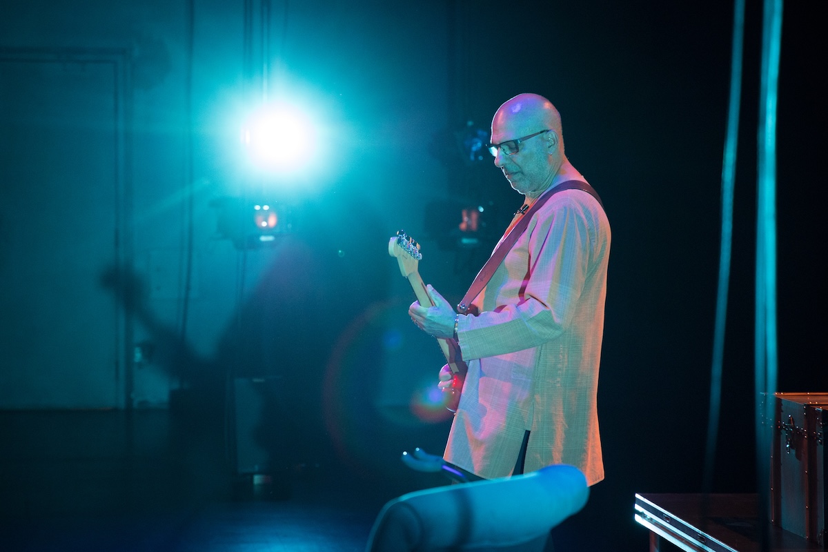 Himmat Singh Shinhat playing guitar during Panj, bathed in teal stage lighting, in profile © Laurence Ly